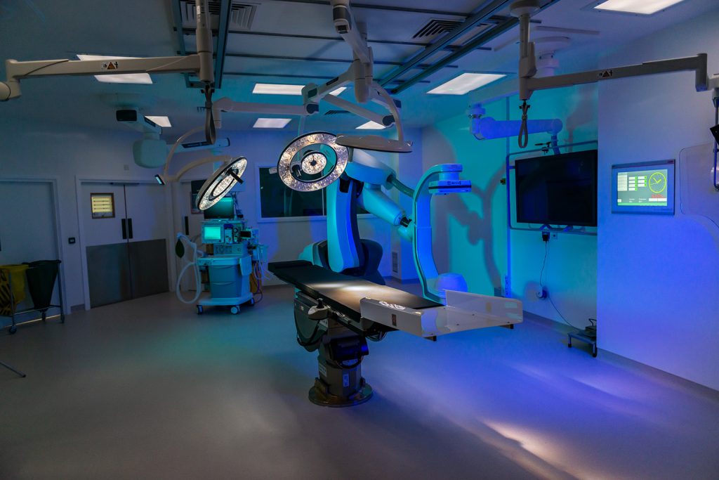 Modern operating theatre with central surgical table, overhead lights, and advanced equipment in a clean, sterile setting.